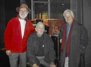 Three older men standing in front of the suitcase exhibition at the Pier 21 Museum.