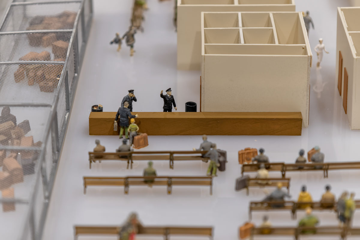 A model of a busy waiting area with two uniformed light-skinned men at a counter.