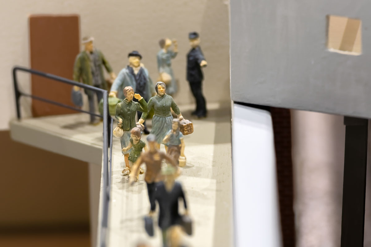 Figurines of a group of four people, including two children, making their way down a ramp amidst a crowd.